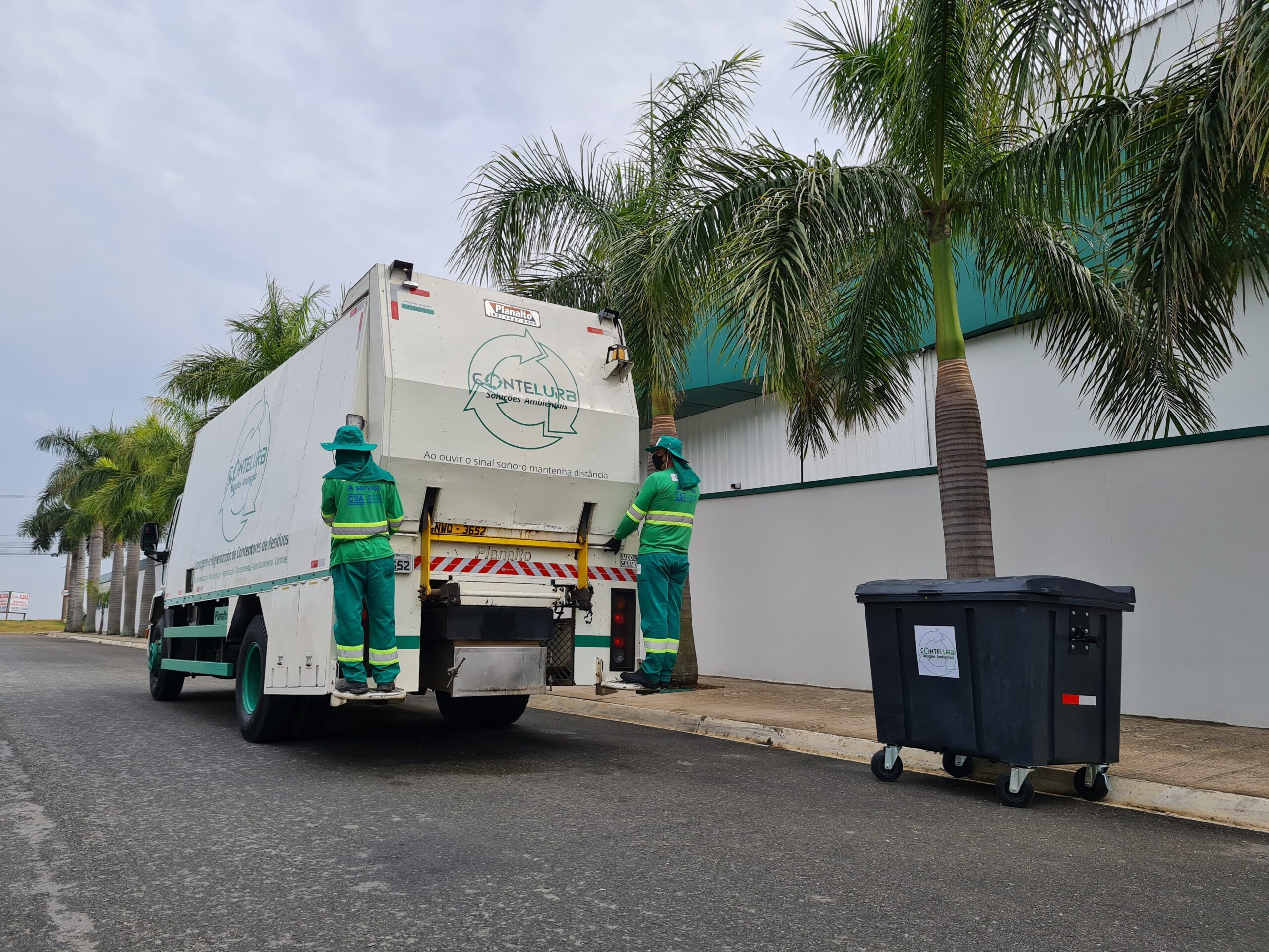 Contêiner de lixo da Contelurb instalado na rua, com um caminhão de higienização de contentores da empresa ao lado.