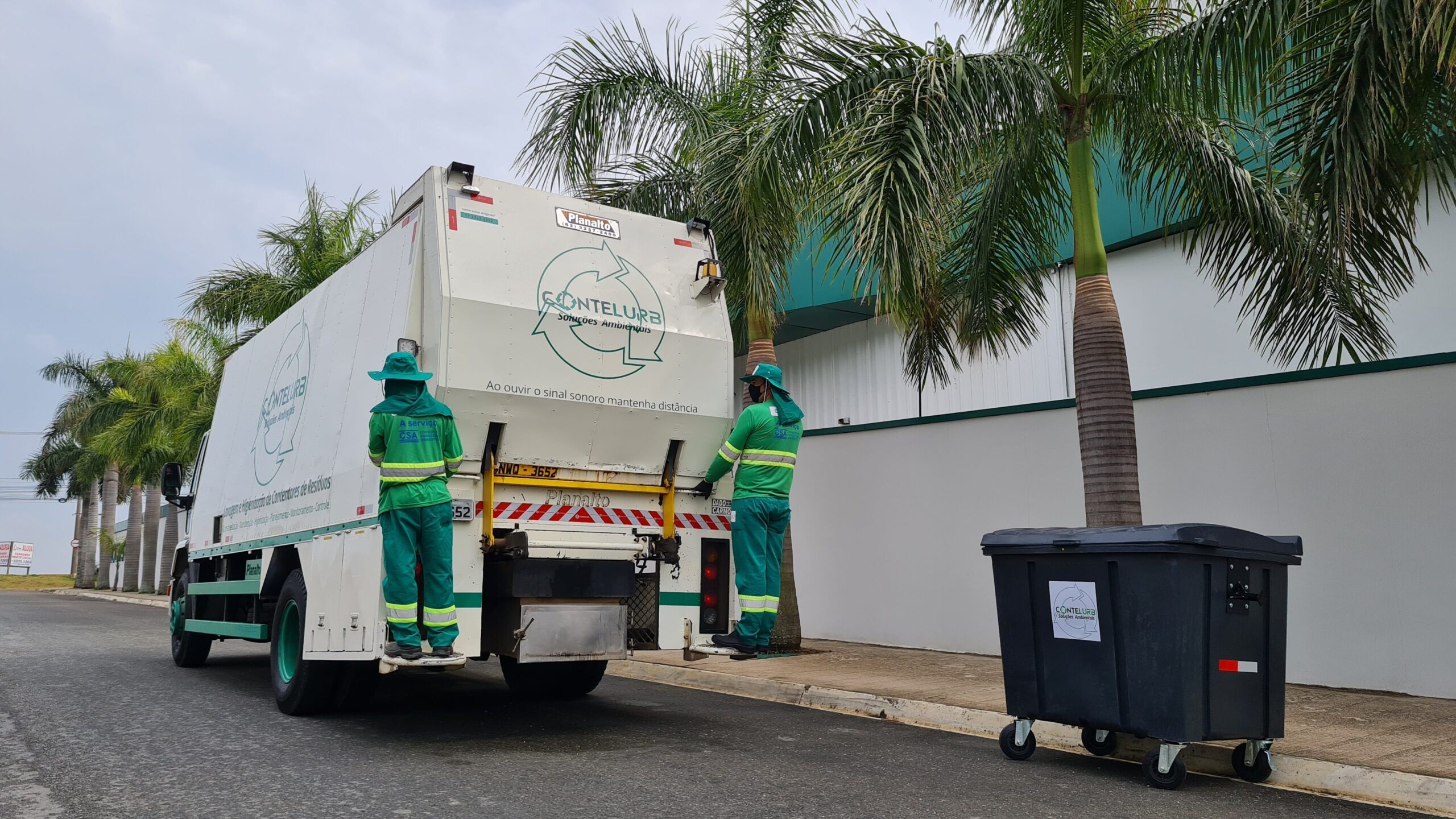 Contêiner de lixo da Contelurb instalado na rua, com um caminhão de higienização de contentores da empresa ao lado.