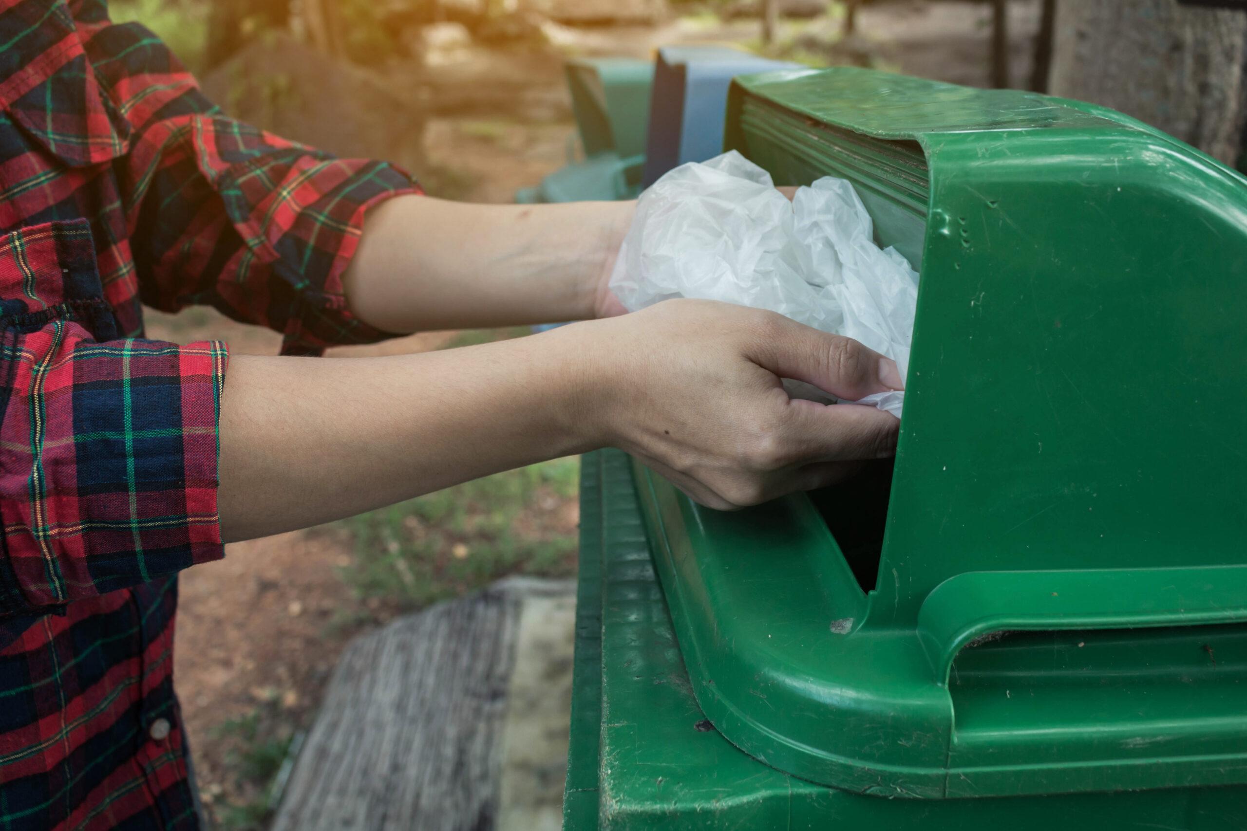 Mulher descartando sacola de plástico em contentor de reciclagem verde para sustentabilidade urbana